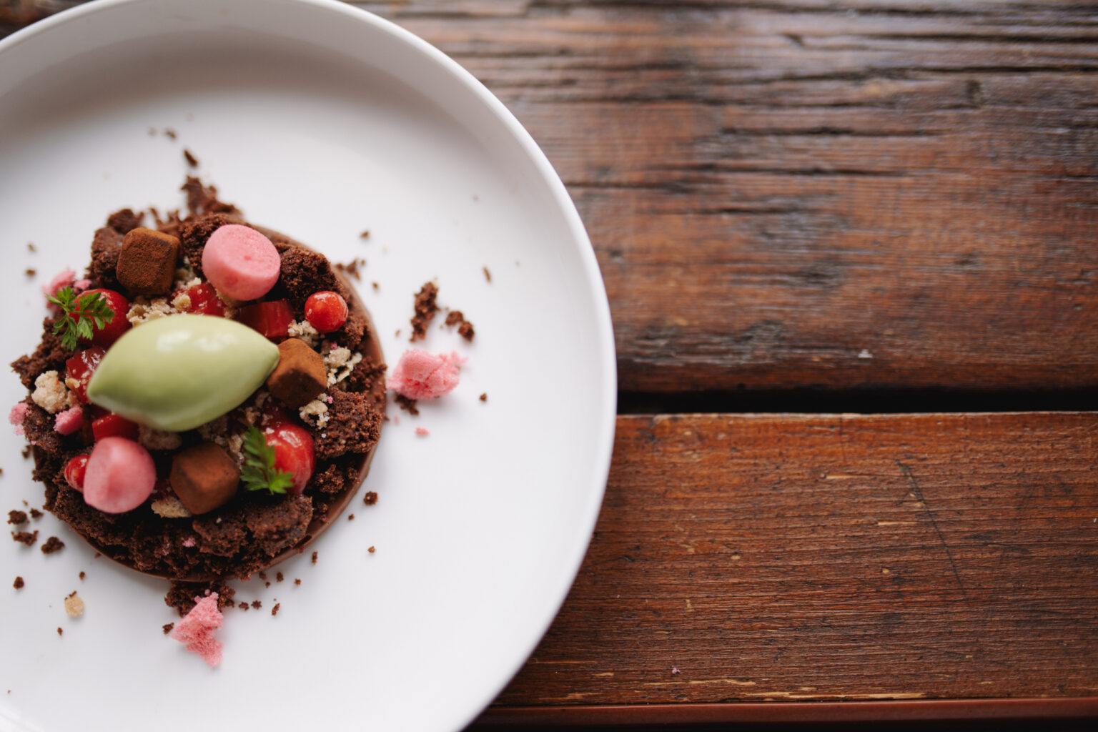 Schokoladendessert mit Erdbeeren, gr&uuml;ner Eisnocke und rosa Baisertupfen