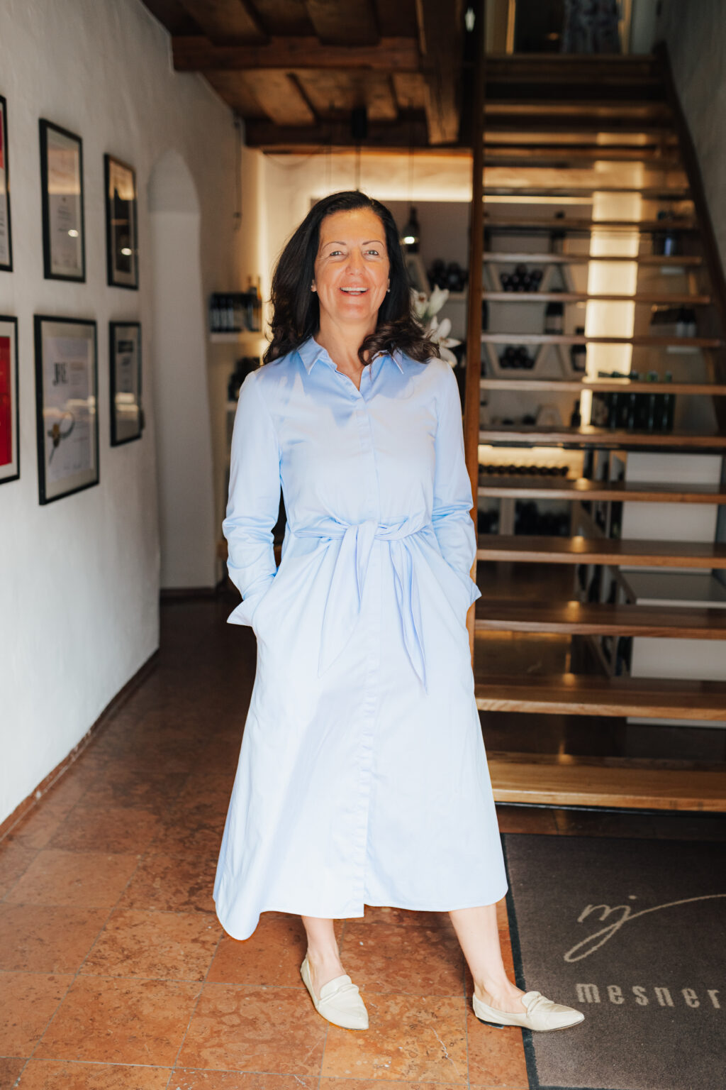 Maria Steffner in einem hellblauen Kleid neben der Innentreppe des Mesnerhauses
