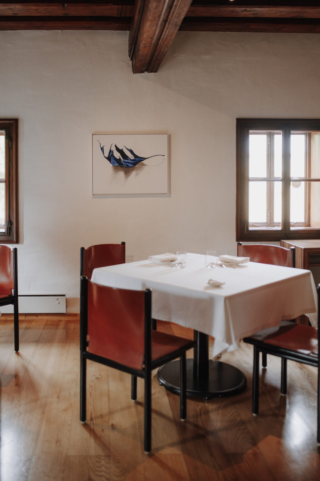 Gedeckter Tisch mit roten St&uuml;hlen und gerahmtem Fischmotiv im Mesnerhaus Gourmet-Restaurant