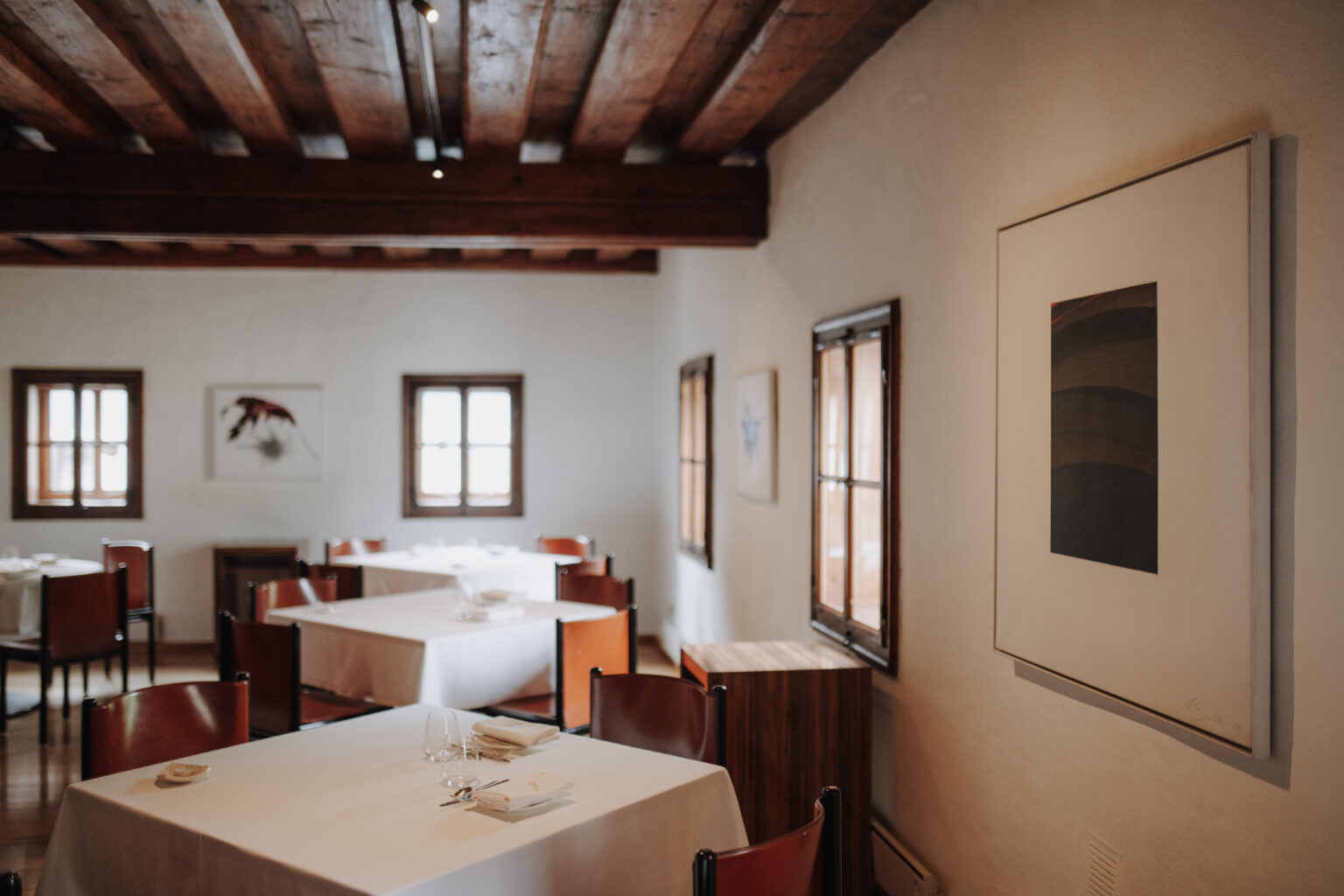 Gastraum des Mesnerhaus Gourmet-Restaurants mit gedeckten Tischen, roten St&uuml;hlen und Kunstwerken