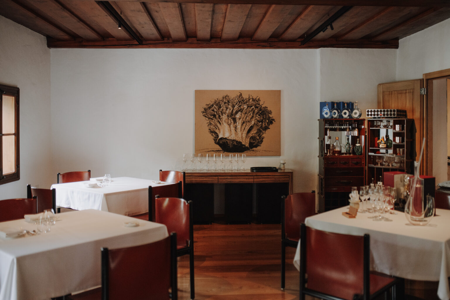 Gedeckte Tische im Mesnerhaus Gourmet-Restaurant vor einem Baum-Kunstwerk und einer Getr&auml;nkevitrine