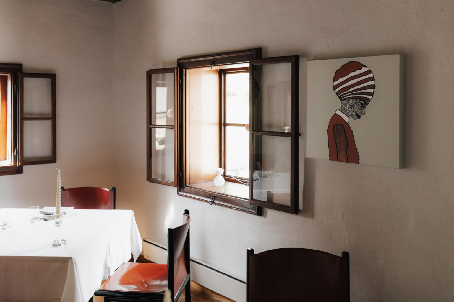 Gedeckter Tisch am offenen Fenster im Mesnerhaus Gourmet-Restaurant mit Portr&auml;tkunst an der Wand