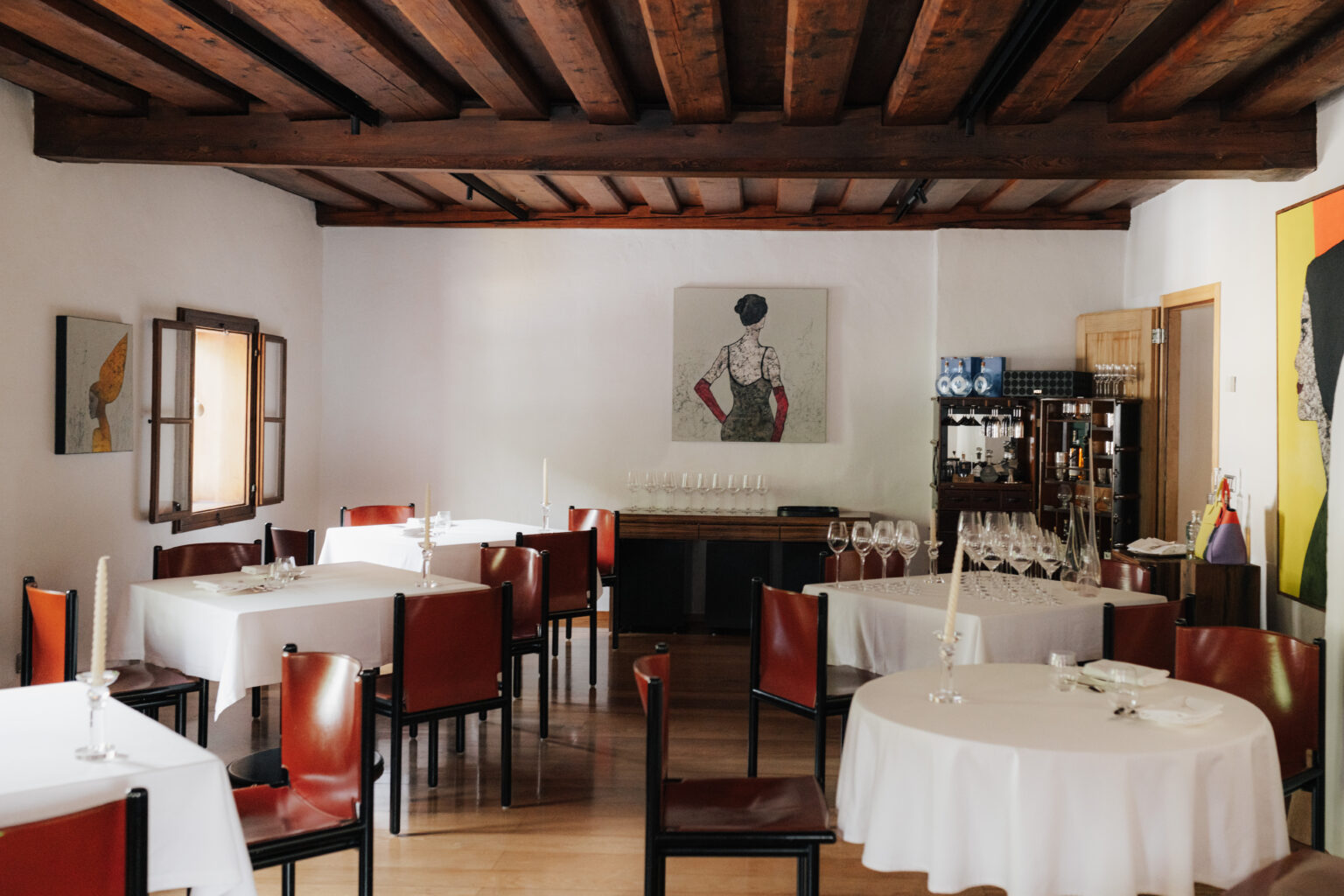Gastraum des Mesnerhaus Gourmet-Restaurants mit wei&szlig;en Tischt&uuml;chern, roten St&uuml;hlen und Kunstwerken