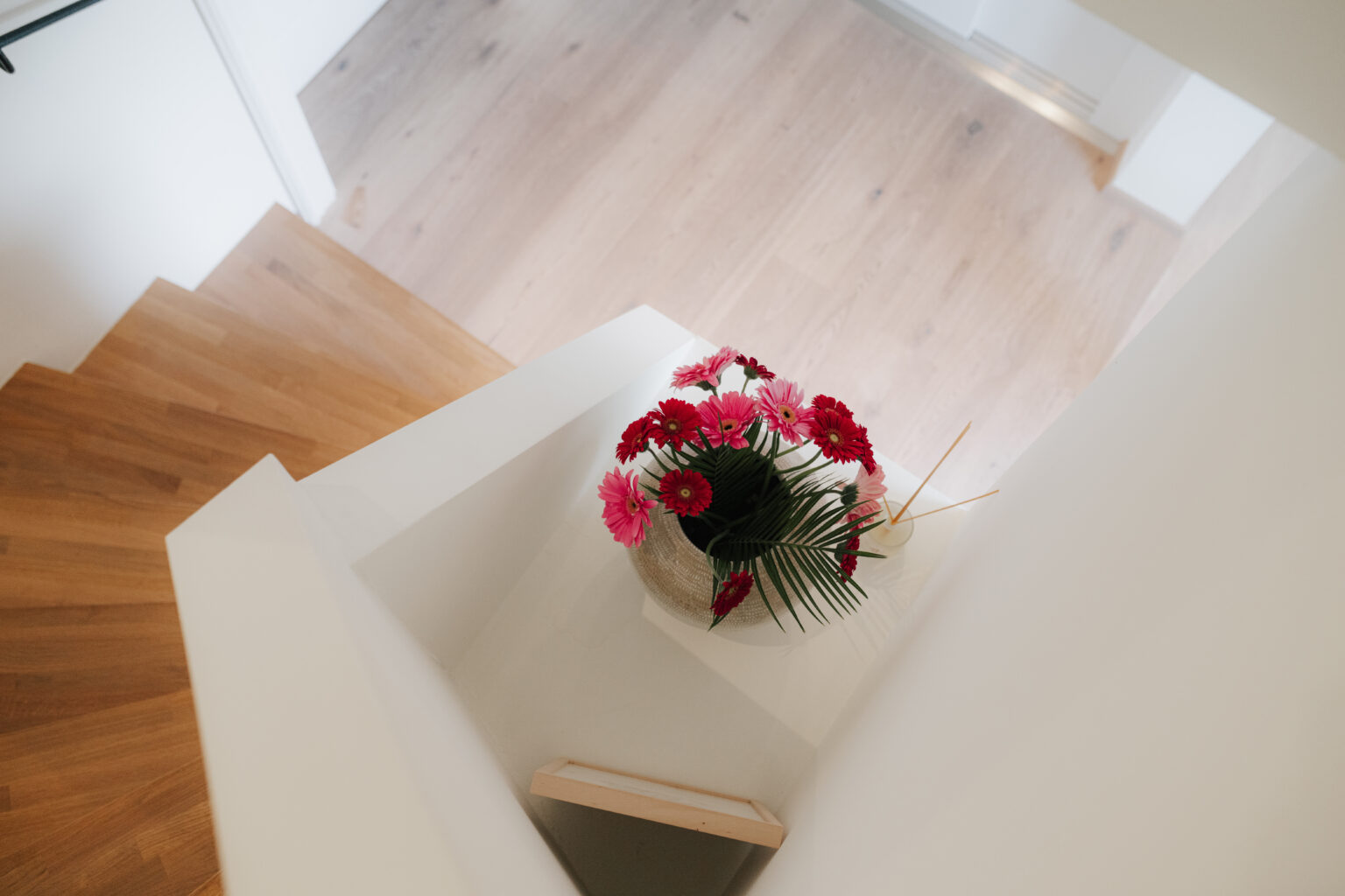 Blick von oben auf die helle Holztreppe im Mesnerhaus mit Blumenschmuck
