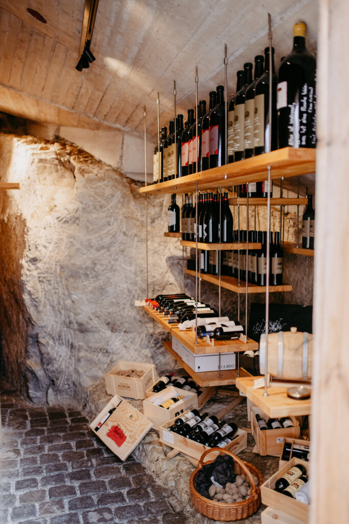 mesnerhaus-weinkeller-03 Weinkeller des Mesnerhauses mit Weinflaschen auf Holzregalen und Natursteinwänden
