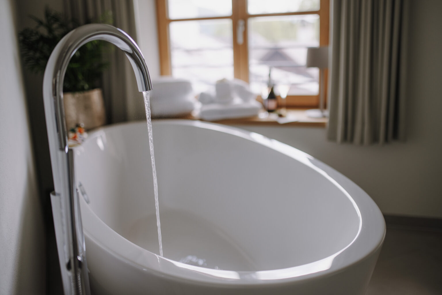 Freistehende Badewanne mit einlaufendem Wasser in einem Zimmer des Mesnerhaus Boutique-Hotels